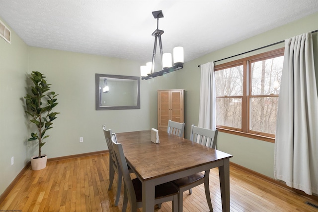 dining area with a notable chandelier, a textured ceiling, and light hardwood / wood-style flooring