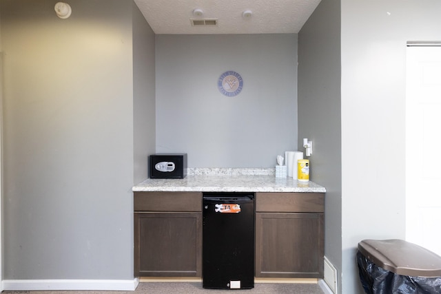 bar featuring dark brown cabinets and a textured ceiling