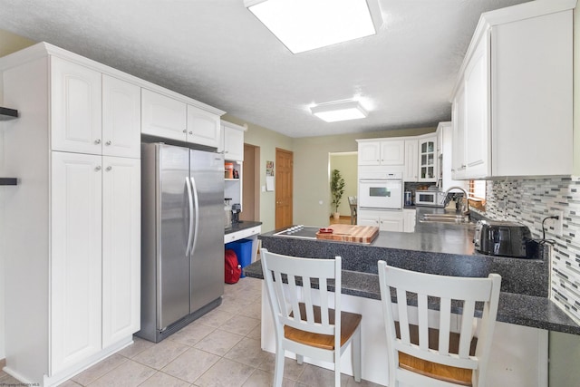 kitchen with sink, light tile patterned floors, stainless steel appliances, white cabinets, and kitchen peninsula