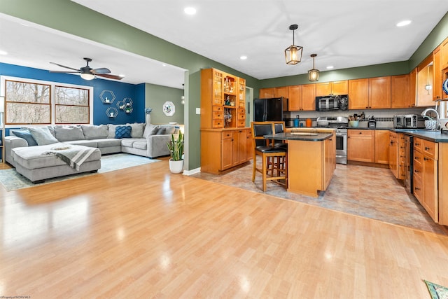 kitchen featuring hanging light fixtures, a center island, light hardwood / wood-style floors, black appliances, and a kitchen bar