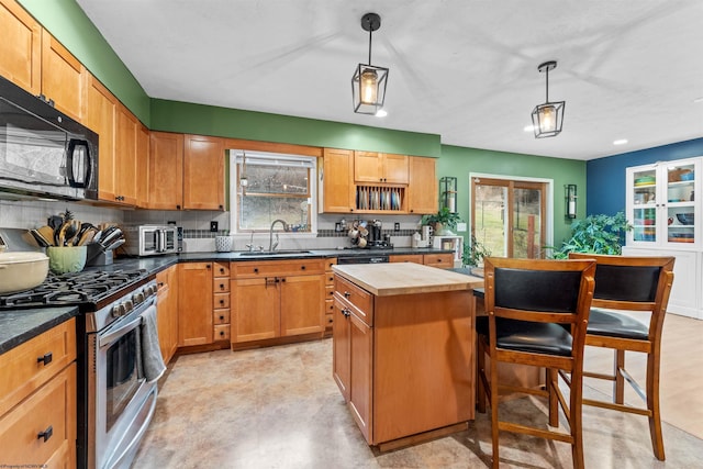 kitchen with pendant lighting, sink, stainless steel gas range, tasteful backsplash, and a kitchen island