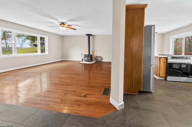 unfurnished living room featuring ceiling fan, dark wood-type flooring, a healthy amount of sunlight, and a wood stove