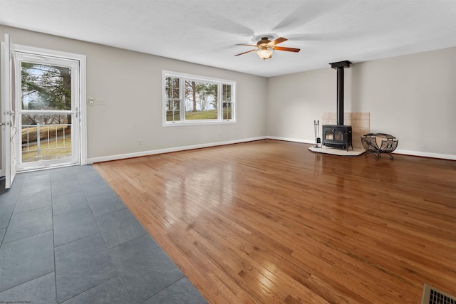 unfurnished living room featuring dark wood-type flooring, ceiling fan, and a wood stove