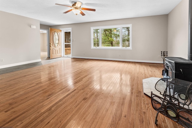 living room with a wood stove, ceiling fan, and light hardwood / wood-style flooring