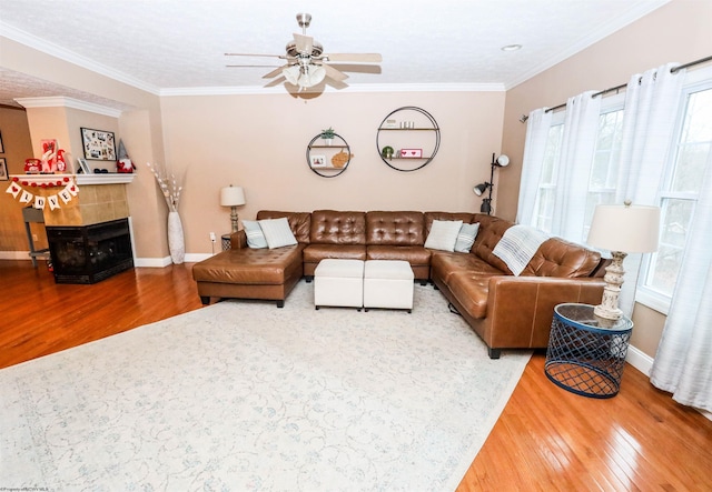 living room featuring a tiled fireplace, ornamental molding, wood-type flooring, and ceiling fan