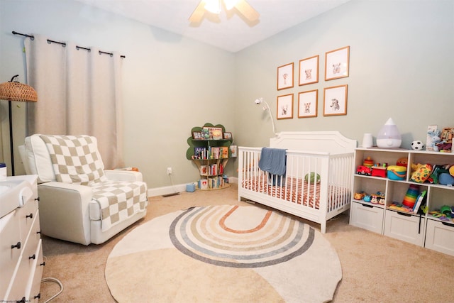 bedroom with light colored carpet, a nursery area, and ceiling fan