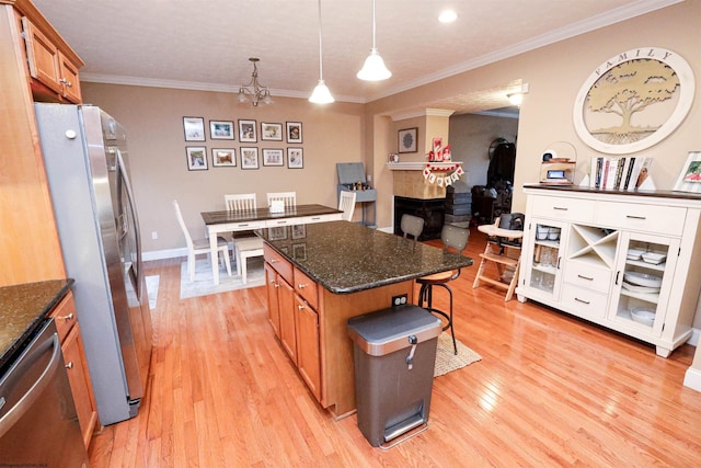 kitchen with appliances with stainless steel finishes, a center island, ornamental molding, light hardwood / wood-style floors, and decorative light fixtures