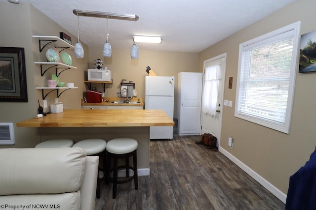 kitchen featuring wood counters, a breakfast bar, hanging light fixtures, kitchen peninsula, and white appliances