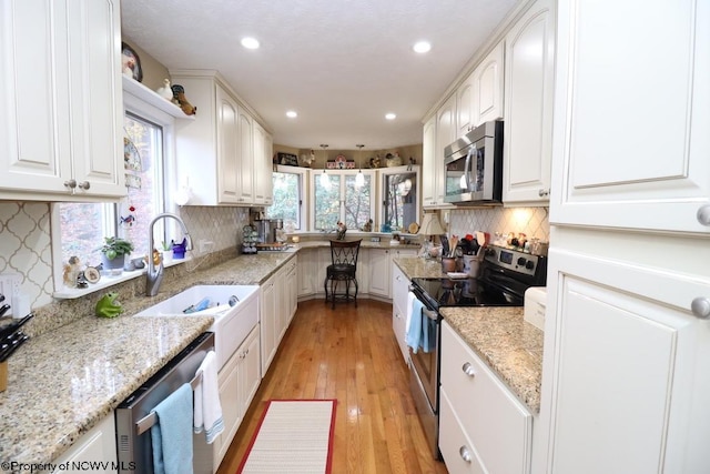 kitchen with tasteful backsplash, stainless steel appliances, light stone countertops, light hardwood / wood-style floors, and white cabinets