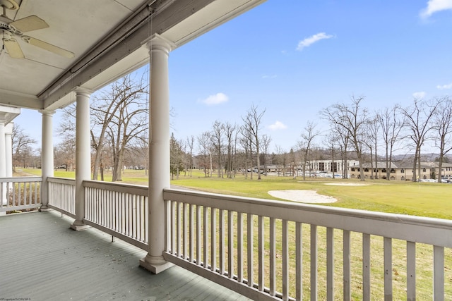 wooden terrace featuring a lawn, ceiling fan, and covered porch