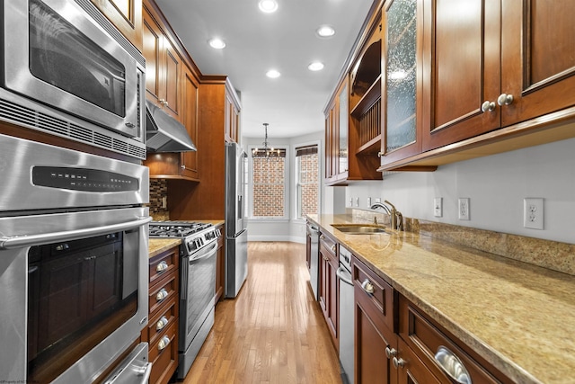 kitchen with sink, light stone counters, light wood-type flooring, pendant lighting, and stainless steel appliances