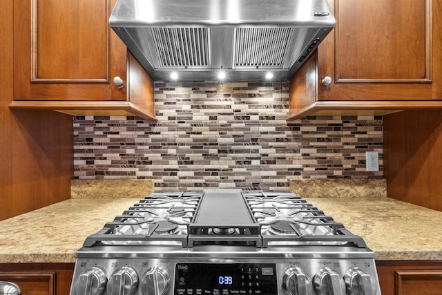 kitchen featuring tasteful backsplash, gas range, light stone countertops, and wall chimney exhaust hood