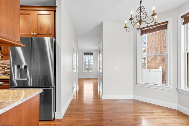 kitchen with stainless steel refrigerator with ice dispenser, hanging light fixtures, a notable chandelier, light hardwood / wood-style floors, and backsplash