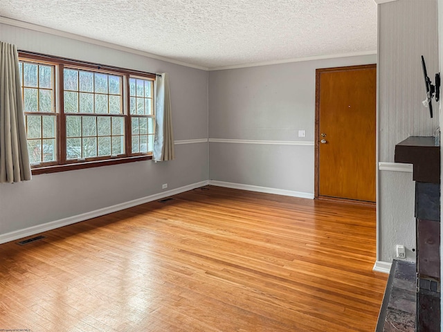 spare room with crown molding, a textured ceiling, and light wood-type flooring