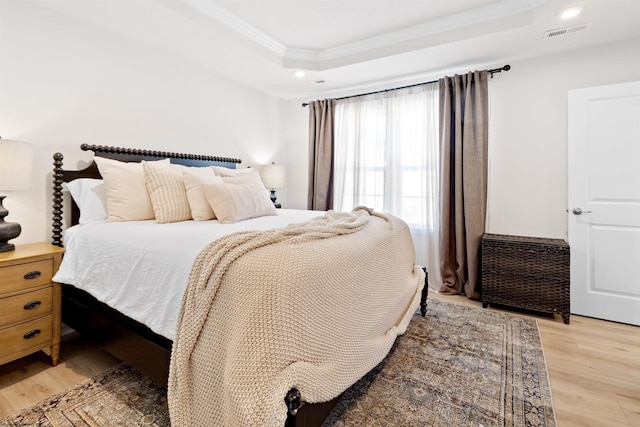 bedroom featuring a raised ceiling, ornamental molding, and light wood-type flooring