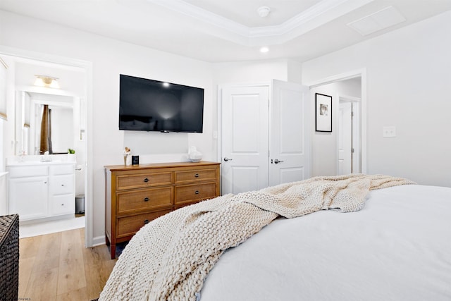 bedroom featuring connected bathroom, light hardwood / wood-style floors, a raised ceiling, crown molding, and a closet