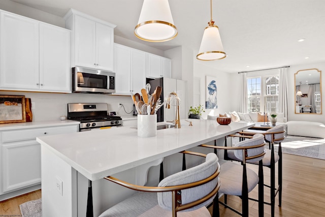 kitchen featuring appliances with stainless steel finishes, decorative light fixtures, white cabinetry, a center island with sink, and light hardwood / wood-style flooring