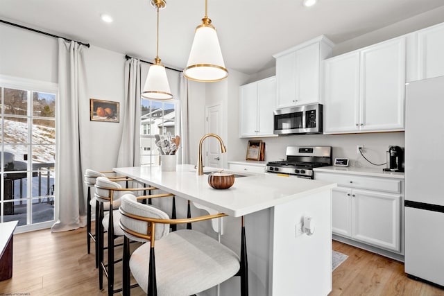 kitchen featuring sink, white cabinetry, a kitchen island with sink, stainless steel appliances, and decorative light fixtures