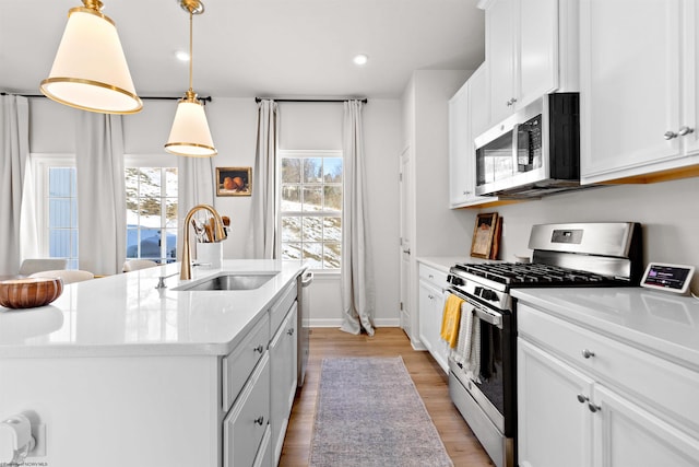 kitchen with appliances with stainless steel finishes, decorative light fixtures, sink, white cabinets, and a kitchen island with sink