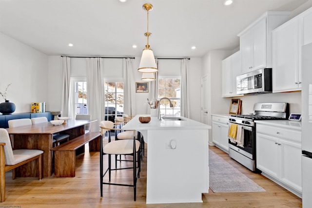 kitchen with sink, stainless steel appliances, an island with sink, white cabinets, and decorative light fixtures