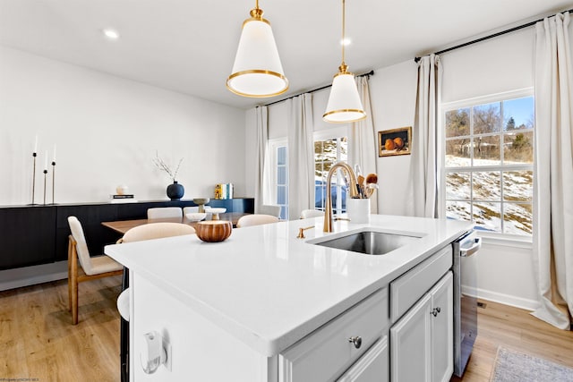 kitchen featuring sink, decorative light fixtures, a center island with sink, light hardwood / wood-style flooring, and white cabinets