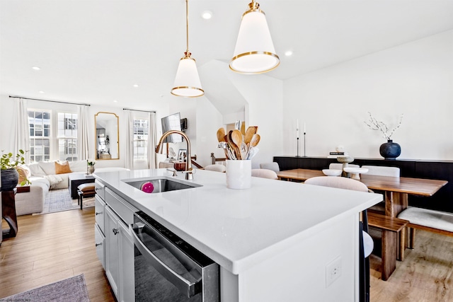 kitchen with sink, hanging light fixtures, light hardwood / wood-style flooring, stainless steel dishwasher, and an island with sink