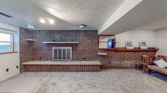 living room with brick wall, a fireplace, carpet, and a textured ceiling