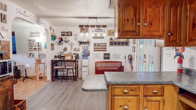 kitchen with decorative light fixtures, kitchen peninsula, a textured ceiling, and light wood-type flooring