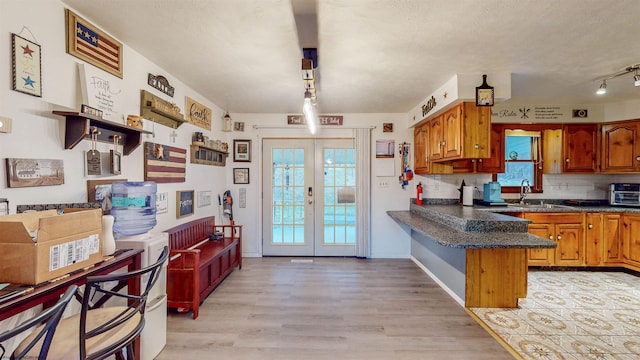 kitchen with sink, tasteful backsplash, french doors, kitchen peninsula, and light wood-type flooring