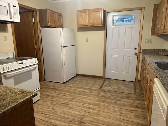 kitchen featuring dark stone countertops, sink, white appliances, and light hardwood / wood-style floors