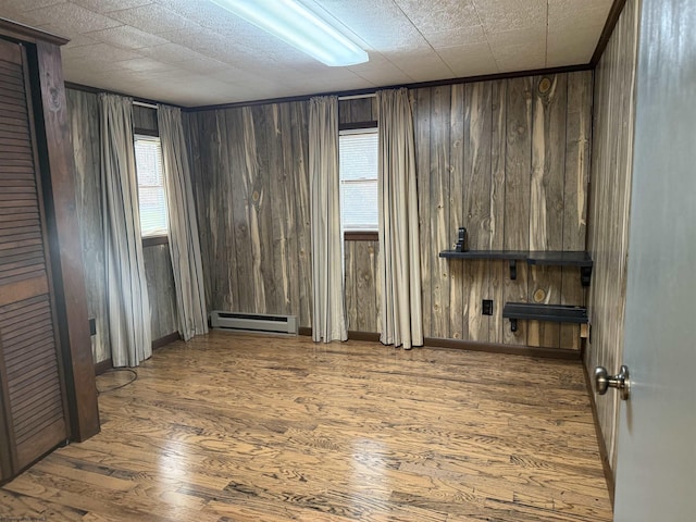 unfurnished room with baseboard heating, plenty of natural light, and wood finished floors