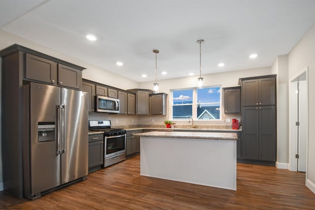 kitchen with pendant lighting, dark hardwood / wood-style flooring, a center island, light stone counters, and stainless steel appliances