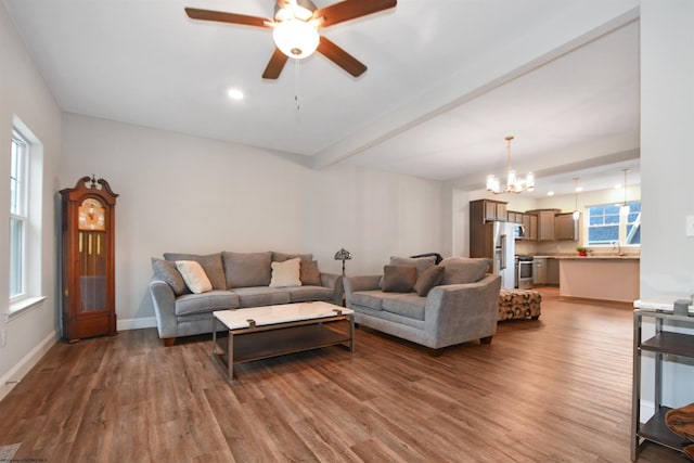 living room featuring sink, beam ceiling, dark wood-type flooring, and ceiling fan with notable chandelier