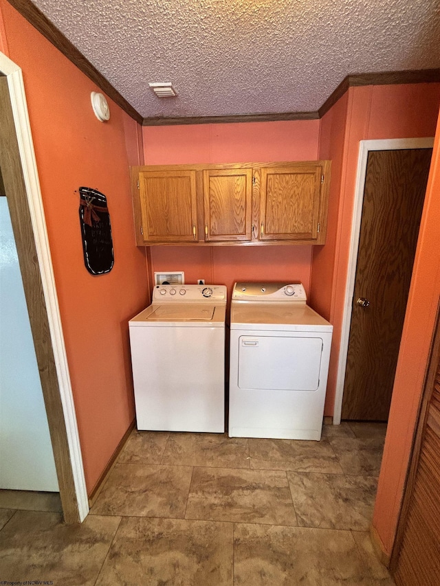 laundry room featuring crown molding, cabinets, a textured ceiling, and washing machine and clothes dryer