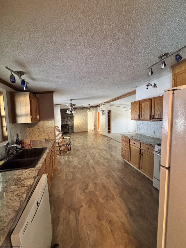 kitchen with sink, white appliances, ceiling fan, light stone counters, and a textured ceiling