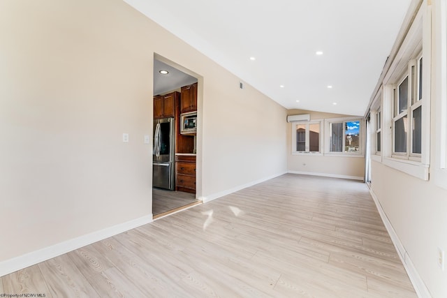 empty room featuring lofted ceiling, a wall mounted air conditioner, and light hardwood / wood-style flooring