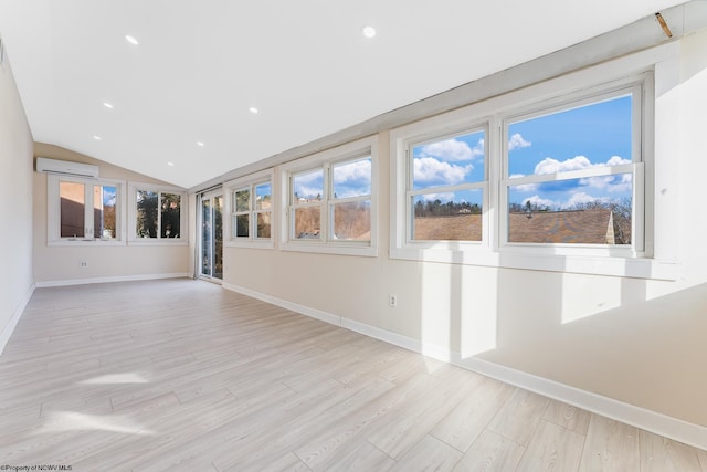 unfurnished living room with vaulted ceiling, a wall mounted air conditioner, light hardwood / wood-style floors, and a wealth of natural light