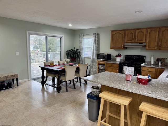 kitchen featuring a breakfast bar, a textured ceiling, light stone counters, and black range with gas cooktop