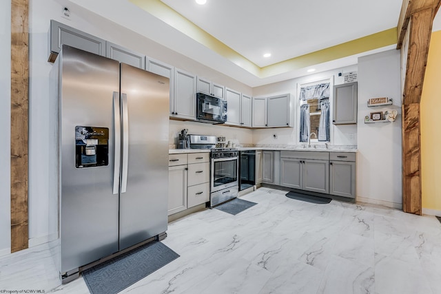 kitchen with stainless steel appliances, a tray ceiling, sink, and gray cabinetry