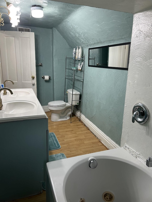 bathroom with lofted ceiling, hardwood / wood-style flooring, vanity, toilet, and a bath