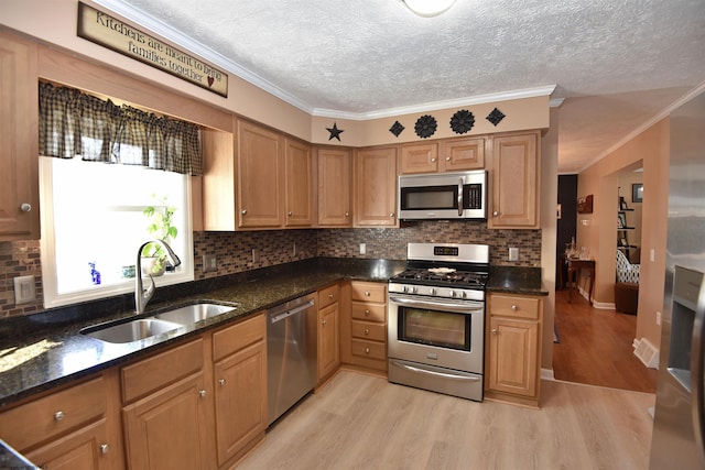 kitchen with stainless steel appliances, sink, dark stone countertops, and light hardwood / wood-style floors