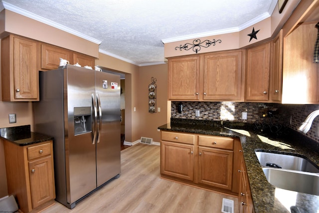 kitchen with ornamental molding, sink, stainless steel fridge, and dark stone counters