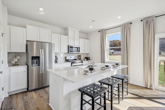 kitchen featuring sink, appliances with stainless steel finishes, white cabinetry, an island with sink, and light wood-type flooring