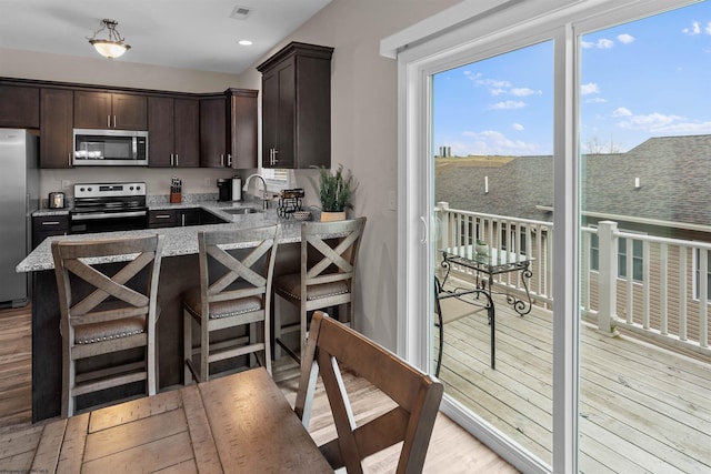 kitchen with sink, a breakfast bar, stainless steel appliances, dark brown cabinetry, and light hardwood / wood-style floors