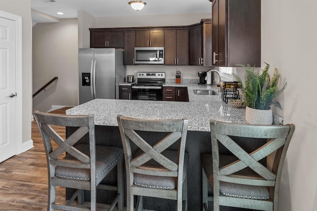 kitchen with sink, dark brown cabinets, appliances with stainless steel finishes, a kitchen breakfast bar, and light stone countertops