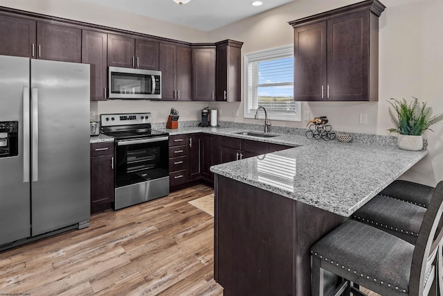 kitchen featuring a kitchen bar, sink, light wood-type flooring, appliances with stainless steel finishes, and kitchen peninsula