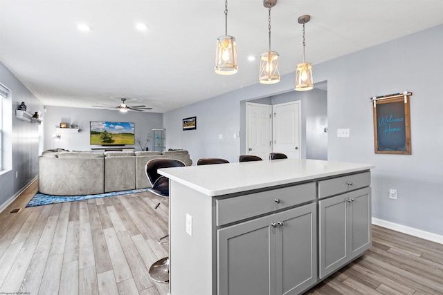 kitchen featuring ceiling fan, gray cabinetry, hanging light fixtures, a kitchen island, and light wood-type flooring