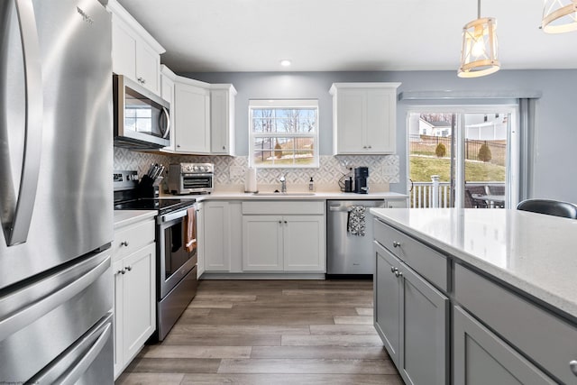 kitchen featuring sink, gray cabinetry, white cabinetry, decorative light fixtures, and appliances with stainless steel finishes