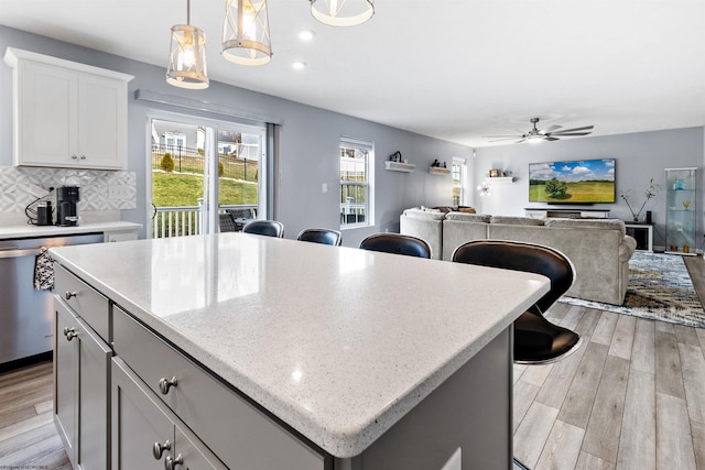 kitchen featuring light hardwood / wood-style flooring, stainless steel dishwasher, a kitchen island, pendant lighting, and decorative backsplash