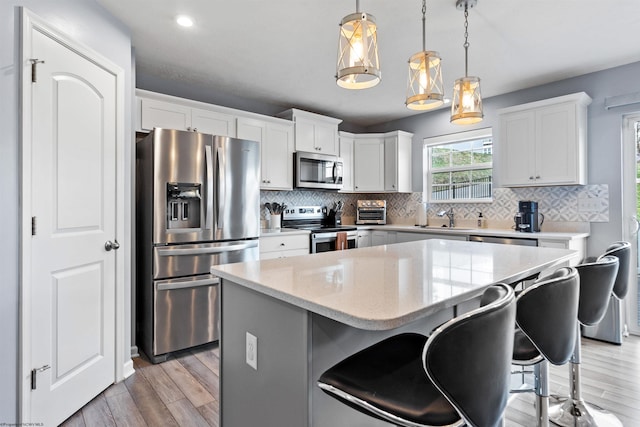 kitchen with appliances with stainless steel finishes, hanging light fixtures, tasteful backsplash, white cabinets, and a kitchen island